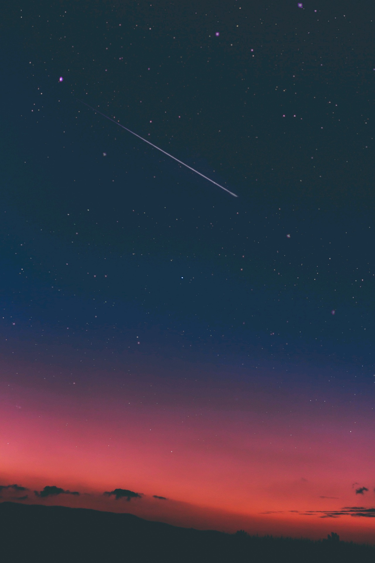 Eine Sternschnuppe am Abendhimmel, schräg von oben nach unten.