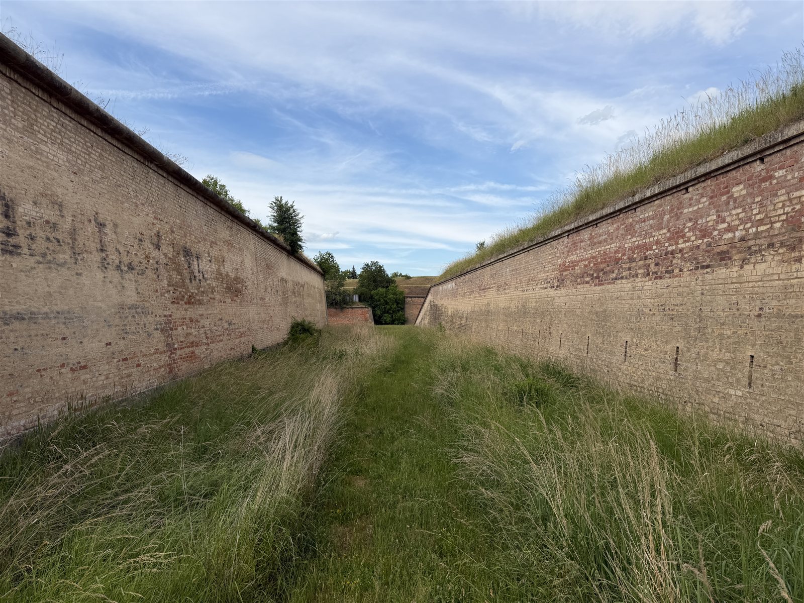 Grasbewachsener Graben zwischen zwei langen Ziegelwällen
