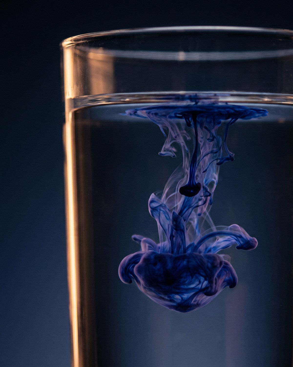 Ein Tropfen dunkelblaue Tinte breitet sich in einem Glas mit stillem Wasser aus