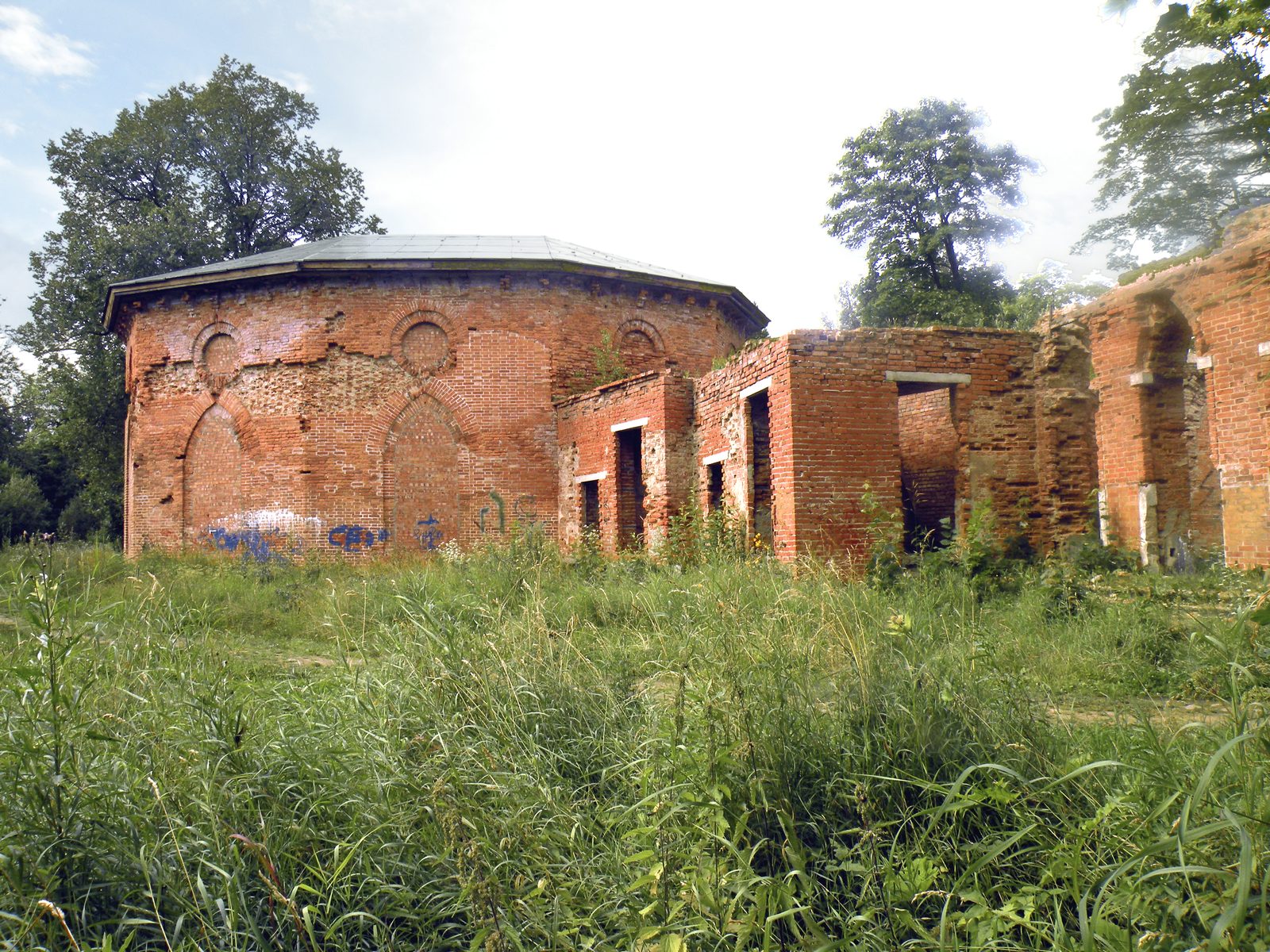 Die Ruine des Babolowo-Palais von außen, rote Ziegelmauern im hohen Gras