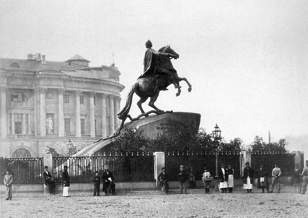 Historische Fotografie: der Eherne Reiter hinter seinem Gitter, davor Passanten