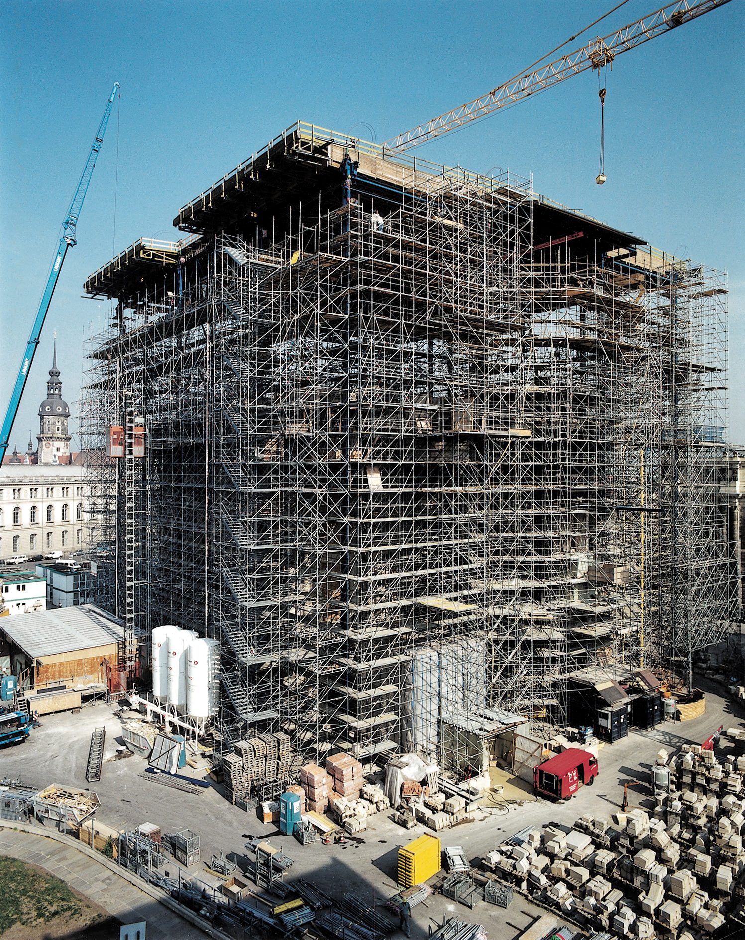 Der Gerüstkubus um die wachsende Frauenkirche mit zwei Kränen, davor das Steinlager