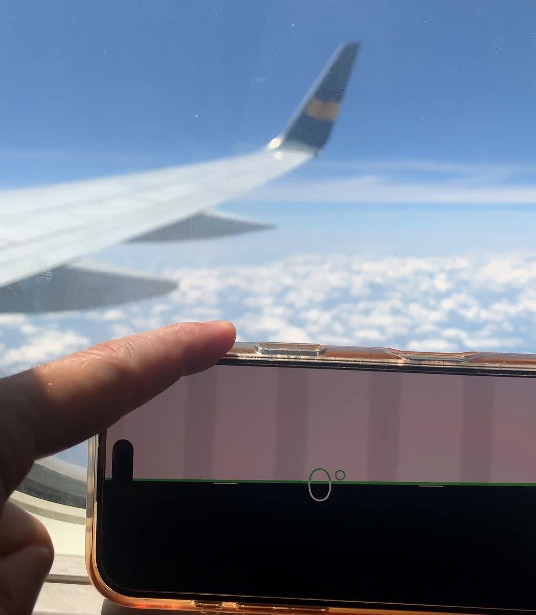 Handy mit Wasserwaage auf dem Fensterrahmen im Flugzeug, draußen Tragfläche, blauer Himmel und Wolkendecke, die Anzeige steht auf 0 Grad