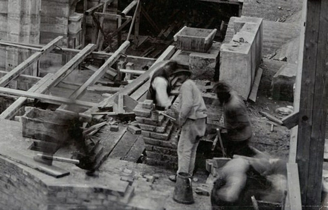 Vergrößerter Ausschnitt: zwei Maurer an einer Ziegelwand der Rathausbaustelle im Mai 1906, daneben verwischte Gestalten.