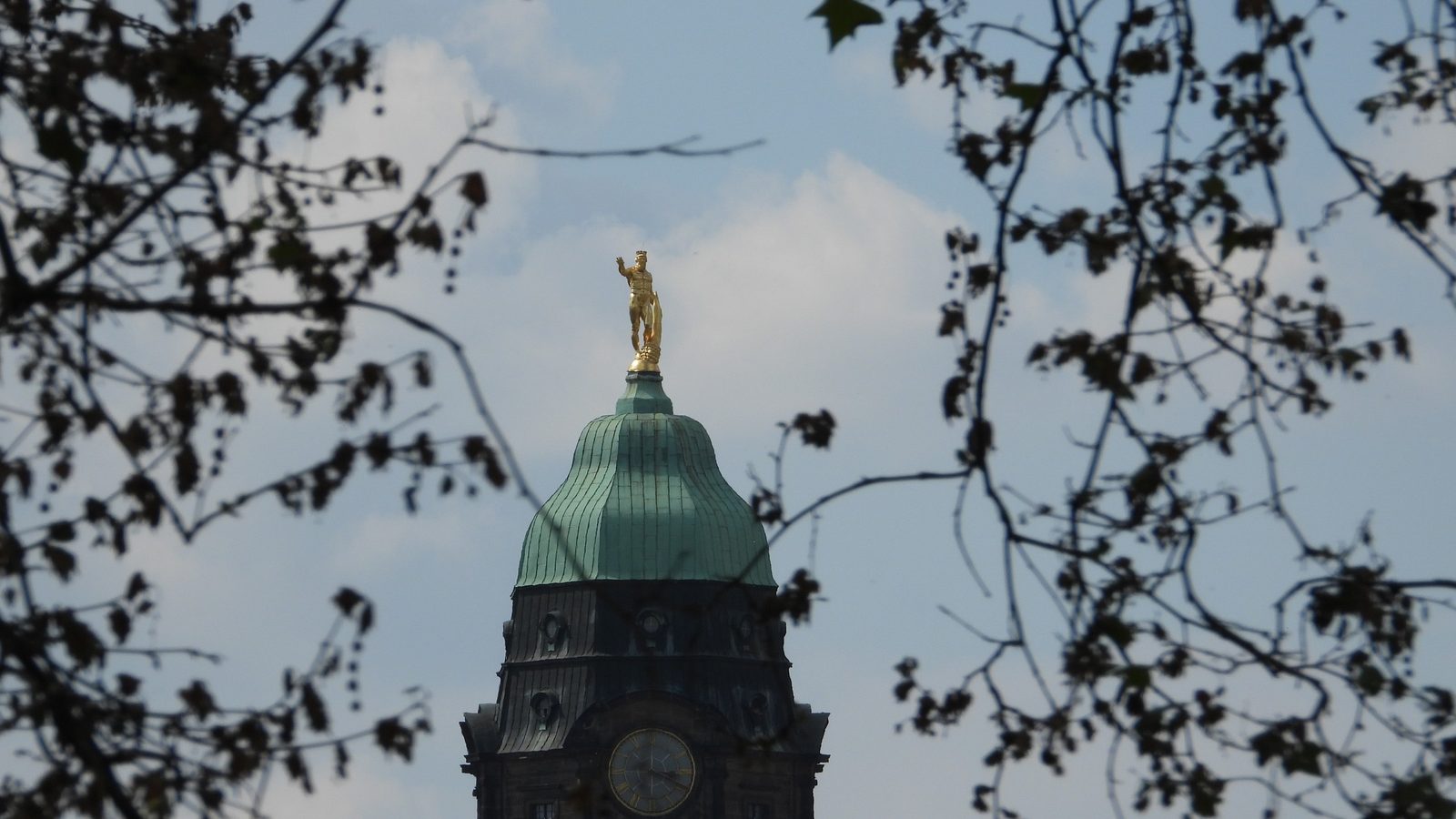 Turmhaube des Neuen Rathauses in Dresden mit Rathausmann und Uhr zwischen kahlen Ästen, 2024.